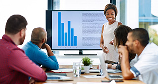 woman presenting to a group in a meeting room with a bar graph on the screen showcasing data trends 2 key points 2 insights